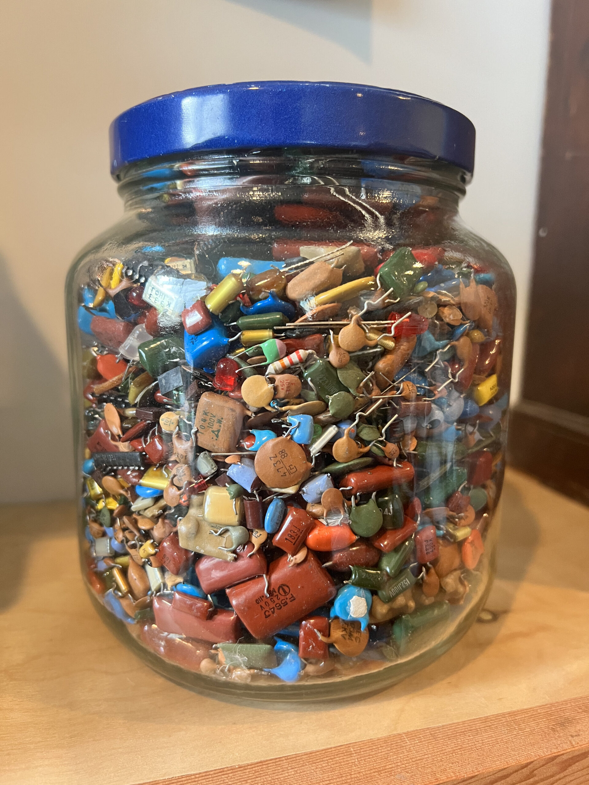 Vintage gallon glass peanut butter jar filled with multicoloured capacitors.