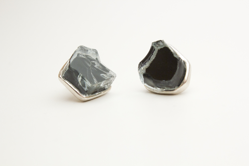 A pair of sterling silver stud earrings set with thick, freeform chunks of black-tinted car glass, set in cast sterling silver bezels.