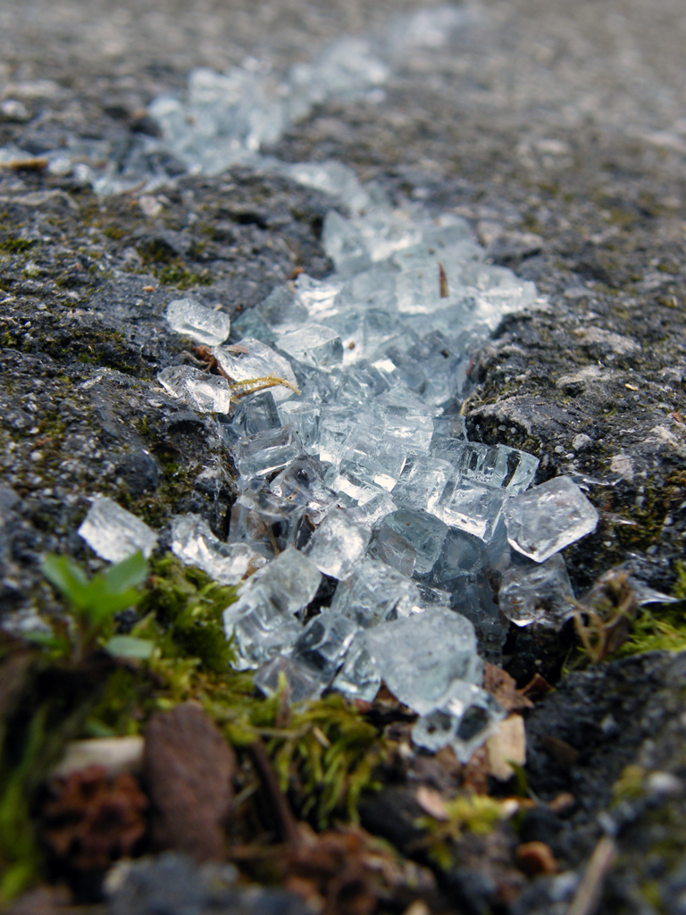 close up sidelong view of a sidewalk fissure filled with clear-white cubes of broken safety glass.
