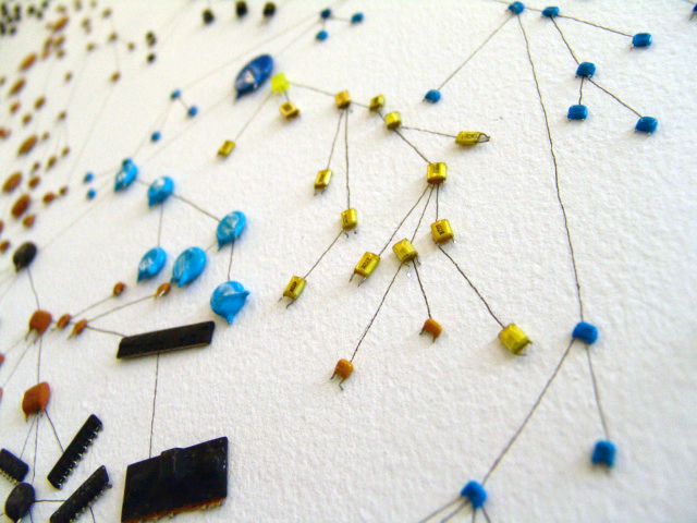 A family tree/tree of life drawn with ink on a wall and populated with electronics components of all shapes and colours.